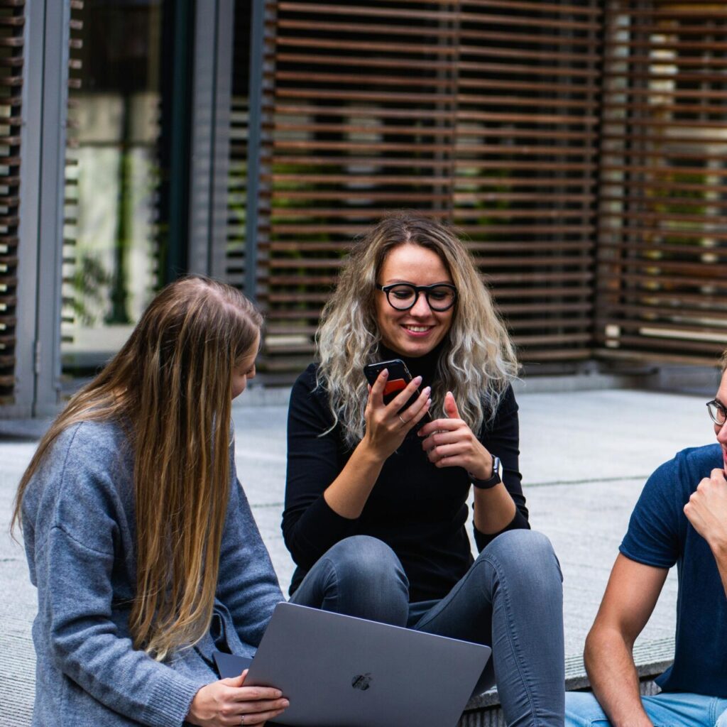 Three young professionals having a friendly chat while sitting on outdoor steps.